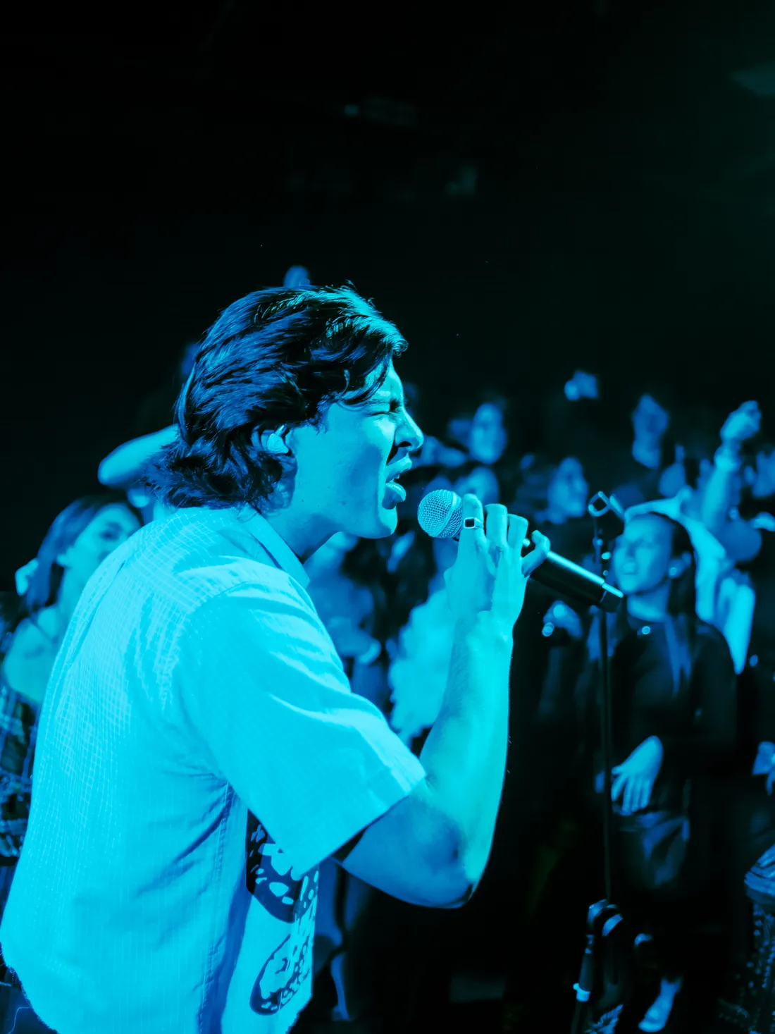 Cantante de perfil bajo luz azul, con el público muy cerca detrás