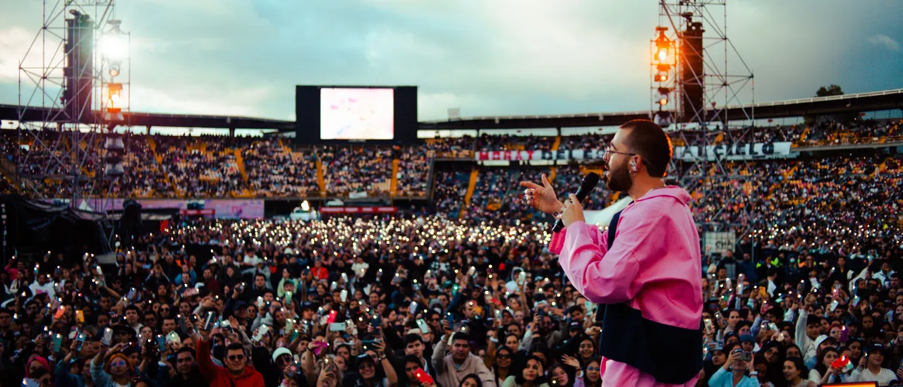 Artista frente a un estadio lleno al atardecer, el público con las linternas encendidas